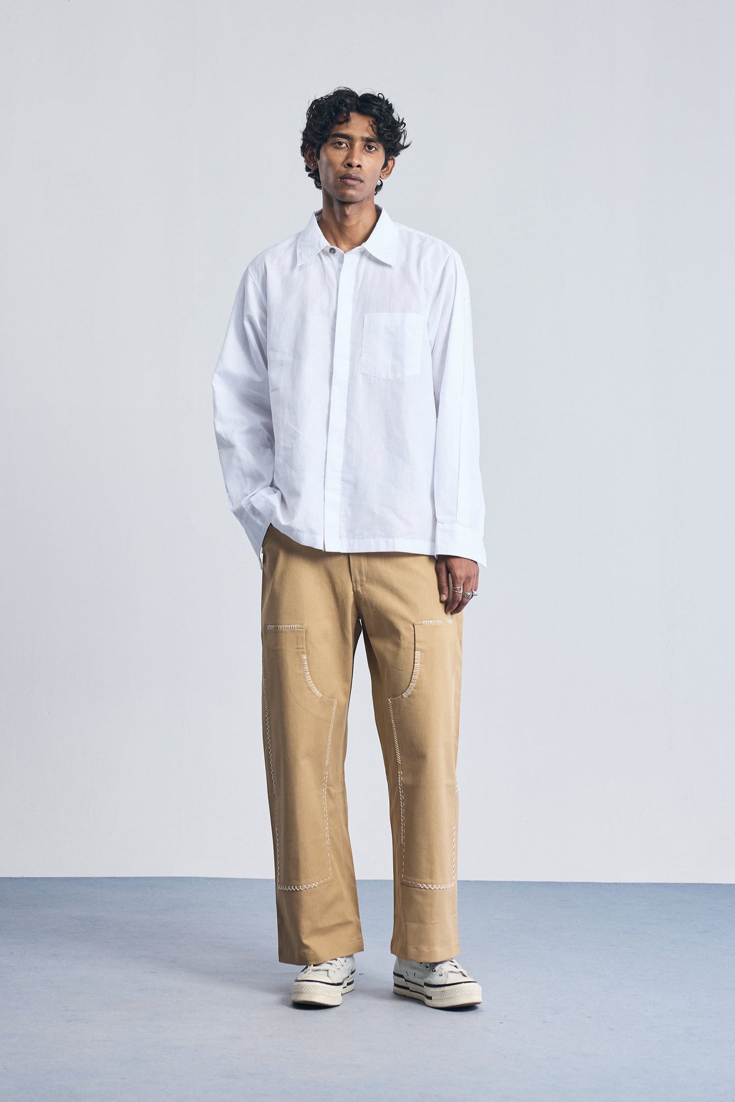 Person wearing a white shirt and beige pants on a plain background